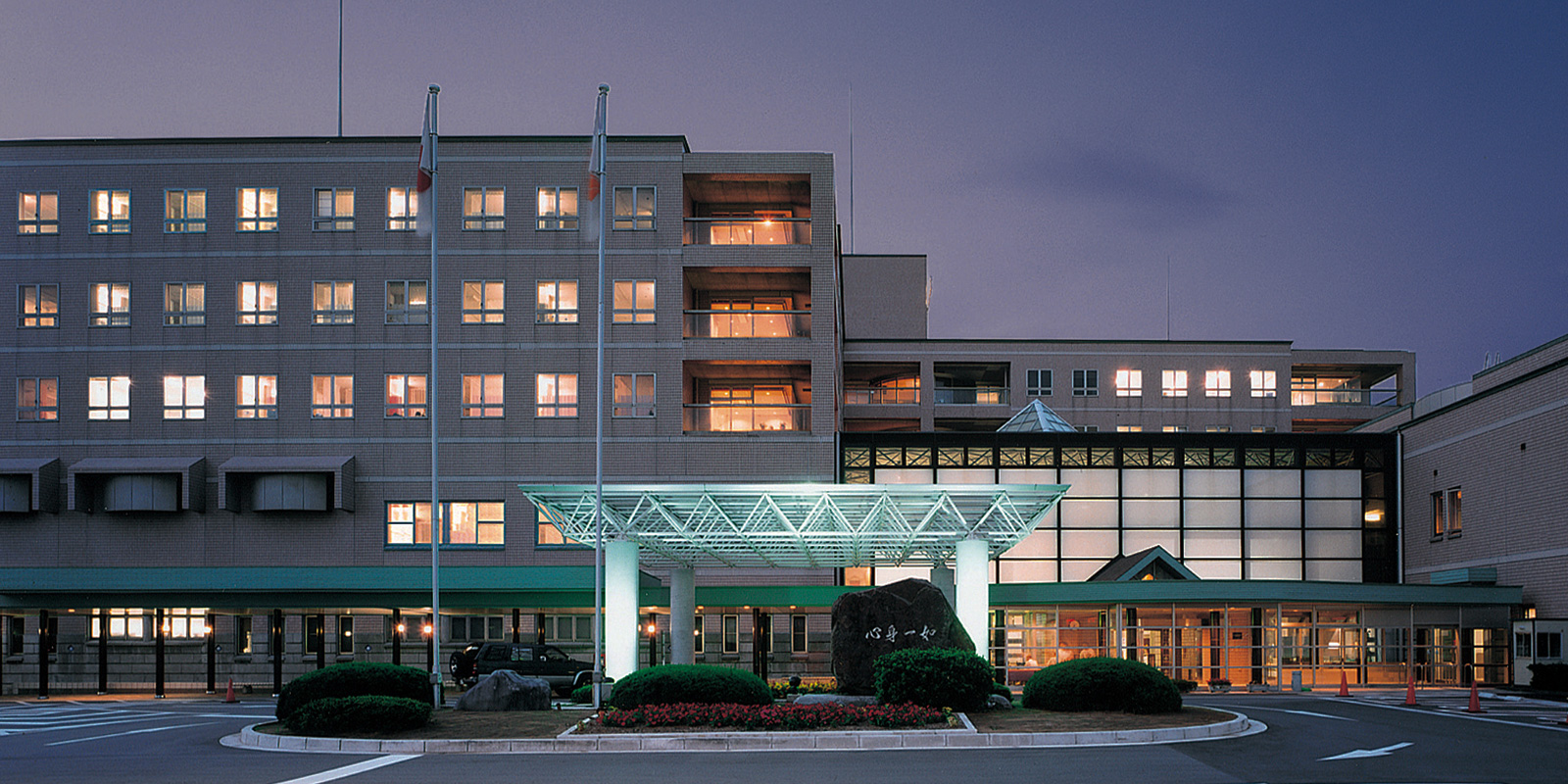 夕暮れ時の介護施設の建物外観。照明が灯った現代的な3階建て施設。