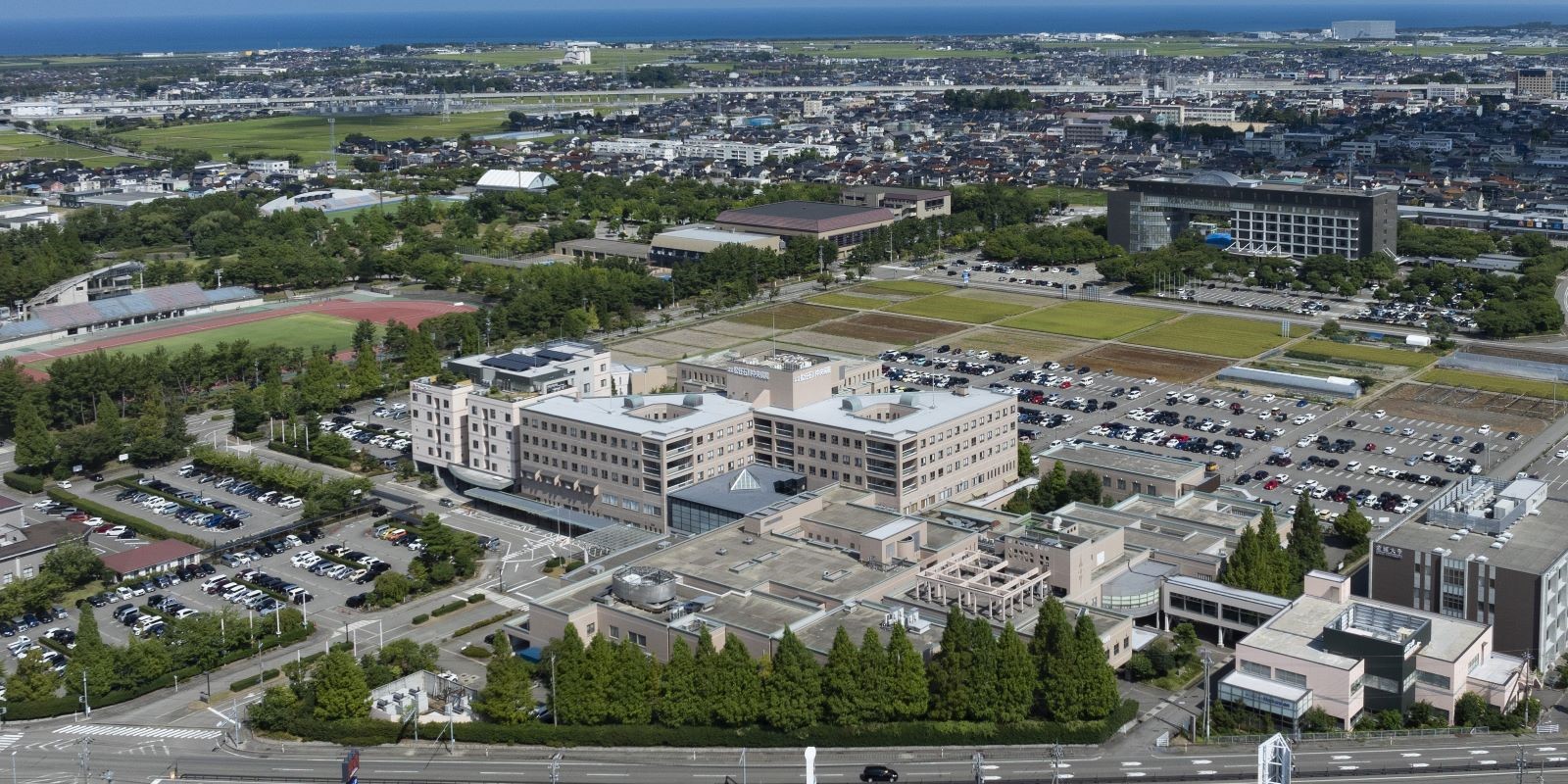 介護施設の広角空撮。複数棟の建物と駐車場、周辺環境が見える